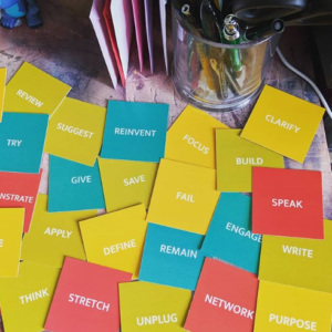 Cards lying flat on a desk with suggestions on marketing a new business - words like stretch, play, speak, purpose and more are in red, green and orange