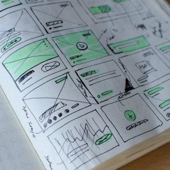 when you need a website you start with drawing wireframes. This is a photo of a sketch pad full of drawn wireframes in pen. They indicate button placement, graphs and where the clicks are