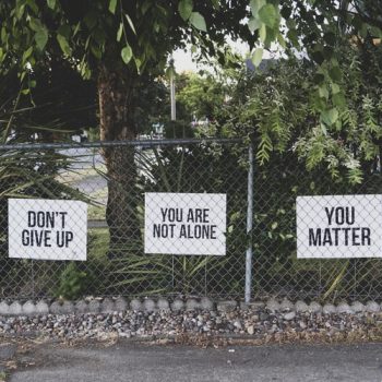 A bunch of signs on a chain link fence read things like you are not alone, don't give up and you matter - they accompany an article on work related suicide