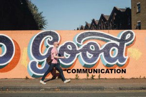 someone walks past a graffiti fence that reads good communication