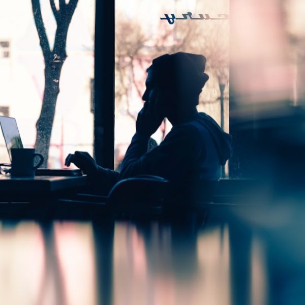 A side profile of a shadowed figure to demonstrate hiring freelancers. This person has a beanie on and looking intently at their laptop in a cafe window.