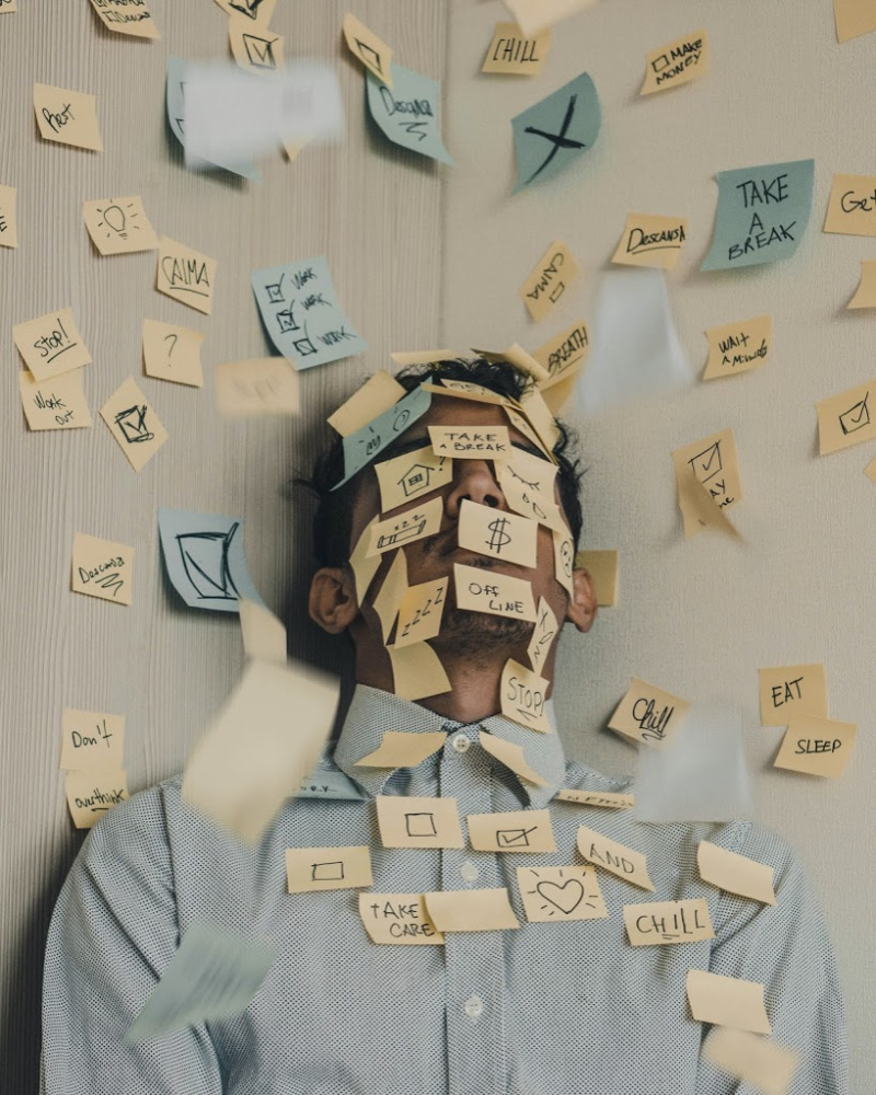 A person in a business shirt with collar has it buttoned to the neck. They are smothered in post-it notes, which obscure their face. This is the epitome of workplace stress, especially in agile team environments