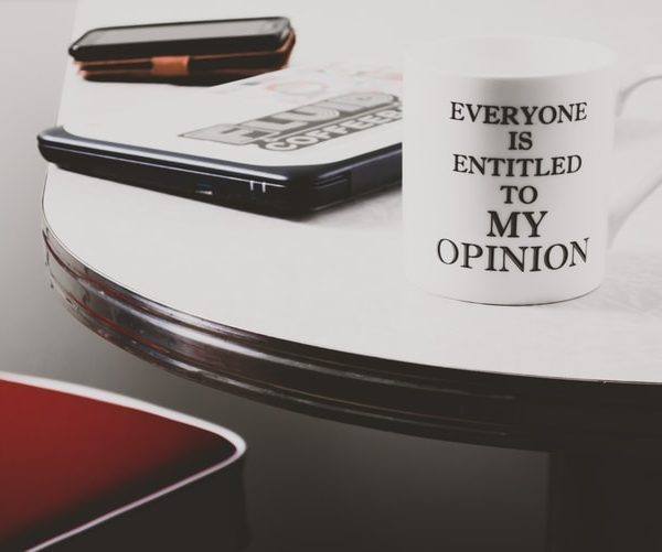 A coffee mug reads everyone is entitled to my opinion. It is on a table. It demonstrates unsolicited advice giving.