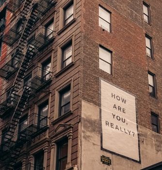 On the side of a brick building in NYC, there is a big poster that reads "how are you really?" In this context, it's meant to allude to mental health in the workplace.