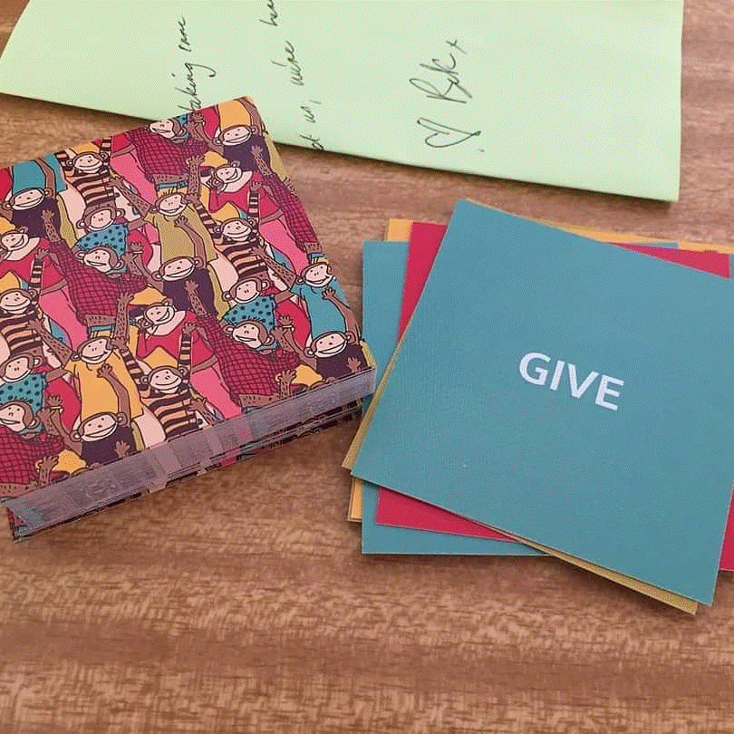 Giving in a mentally healthy workplace is essential. A set of cards on a desk reads give in one side and has small jungle print cartoon animals on the other