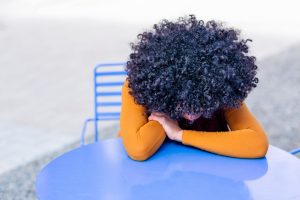 A woman with dark curly hair has her head forlornly on the table